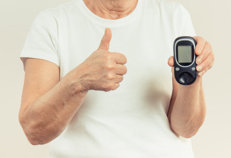 Elderly senior woman holding glucometer for measuring or checking sugar level and showing thumb up. Diabetes in old age conceptの写真素材