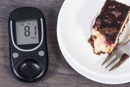 Glucometer with result of measurement sugar level and pieces of fresh baked cheesecake with cherries and chocolate. Nutrition during diabetes conceptの写真素材