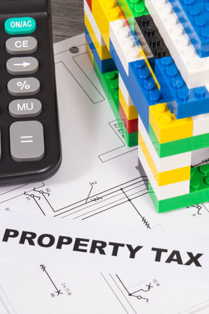 Inscription property tax with small house made of colorful toy blocks and calculator. Increasing real estate or luxury taxation. Tax paymentsの写真素材