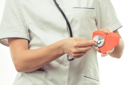 Hand of woman doctor with medical stethoscope examining red heart made of paper. Health care and treatment conceptの写真素材