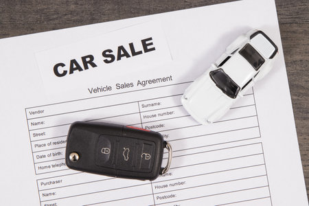 Small white toy car, black car key and vehicle sales agreement. Inscription car sale. Sales or purchases of automobiles. Transportationの写真素材