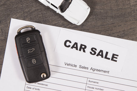 Small white toy car, black car key and form of vehicle sales agreement. Inscription car sale. Sales or purchases new or used vehicle. Transportationの写真素材