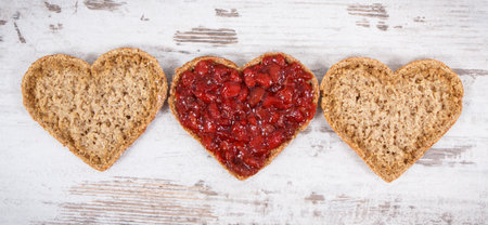 Slice of wholegrain bread with strawberry jam for breakfast. Shape of heart. Old rustic backgroundの写真素材