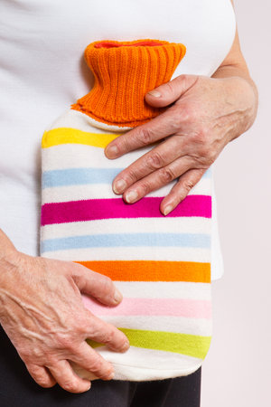 Elderly senior woman with hot water bottle on her stomach. Help with pain in old age. Health careの写真素材