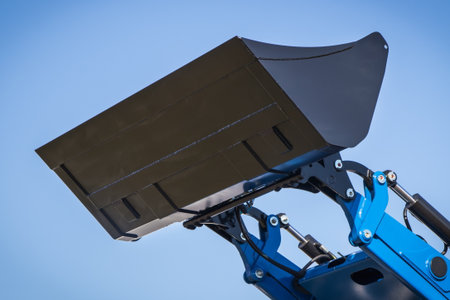 Shovel of excavator or bulldozer on blue sky background. Hydraulic and pneumatic mechanism. Part of...