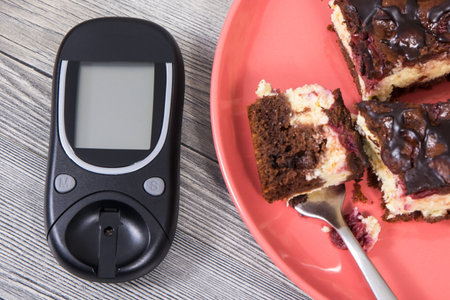 Glucose meter using for measuring sugar level and pieces of fresh baked cheesecake with cherries and chocolate. Nutrition during diabetes conceptの写真素材