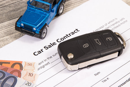 Form of car sale agreement, small blue toy car and black key. Sales and purchases new or used...
