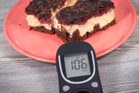 Glucose meter with result of measurement sugar level and pieces of fresh baked cheesecake with cherries and chocolate. Nutrition during diabetes conceptの写真素材