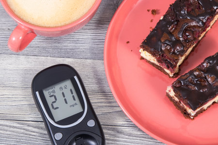 Glucose meter with high result of measurement sugar level, pieces of cheesecake with cherries and chocolate, coffee with milk. Nutrition during diabetes conceptの写真素材