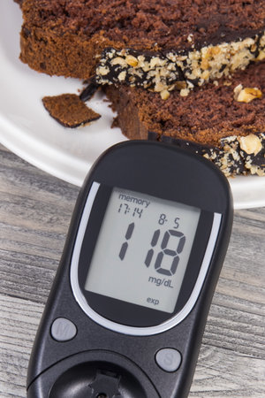 Glucose meter with result of measurement sugar level, sweet chocolate cake. Measuring and checking sugar level during diabetesの写真素材