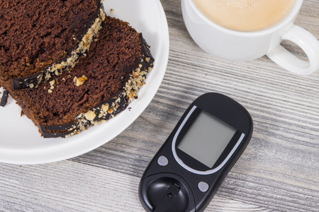 Glucose meter, sweet chocolate cake and cup of coffee with milk. Measuring and checking sugar level during diabetesの写真素材