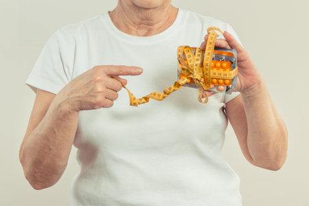 Elderly senior woman with blister packs of vitamins or supplements and centimeter in hand. Treatment, slimming or strengthening immunity in old age. Health careの写真素材