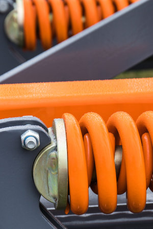 Orange hard spring made of steel. Detail and part of big industrial or agricultural machine....