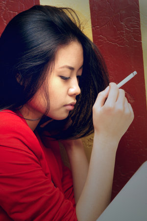 the asian girl thoughtfully sits with a cigaretteの写真素材