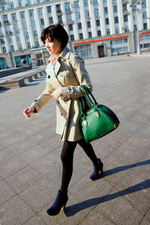 Girl in a light raincoat and green bag, walking down the street.の写真素材