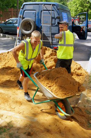 MOSCOW, RUSSIA - JUNE , 2011: A young worker in overalls is transporting sand in a hand-held wheelbarrow. Program for the improvement of public areas in Moscow.のeditorial素材
