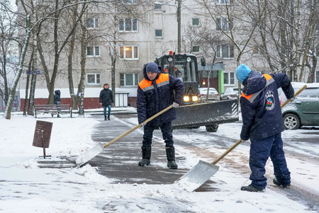 Moscow - January 2020: Workers in uniform with big shovels, a tractor removes snow from the road. Snow removal on the city streets.のeditorial素材