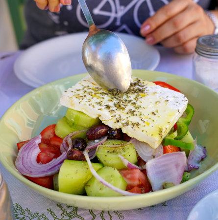 Greek salad of vegetables and cheese. A woman puts a salad in a spoon on her plate.の写真素材