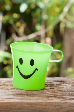Green plastic cup with a smile pasted on wood.の写真素材