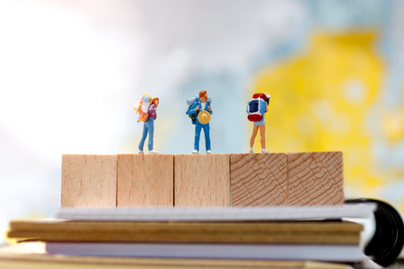 Miniature backpacker standing on wooden block and book, travel and business concept.の写真素材