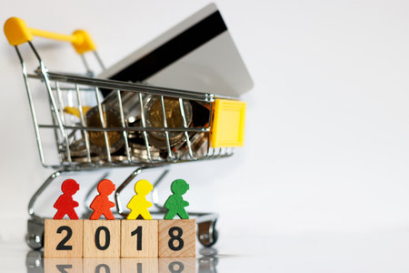 Miniature people: colorful figures standing on wooden number 2018 with shopping cart with coins and credit card.の写真素材