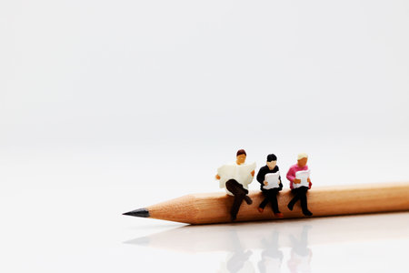 Concept of education and business. Miniature business team sitting on pencil and book use in background or wallpaper.の写真素材