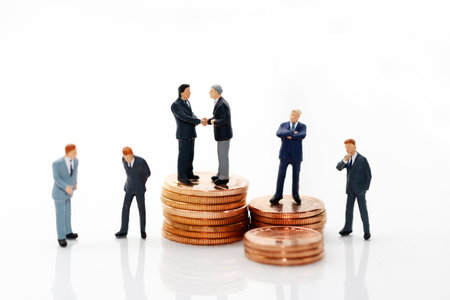 Miniature people: Businessman handshake with coins stack.  Investment, agreement, partnership and business conceptの写真素材