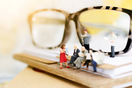 Miniature people reading and sitting on book with glasses using as background, education or business...