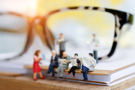 Miniature people reading and sitting on book with glasses using as background, education or business concept.の写真素材