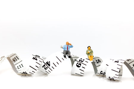 Miniature people: Fat people sitting on measure tape . Healthy lifestyle, dieting and obesity...
