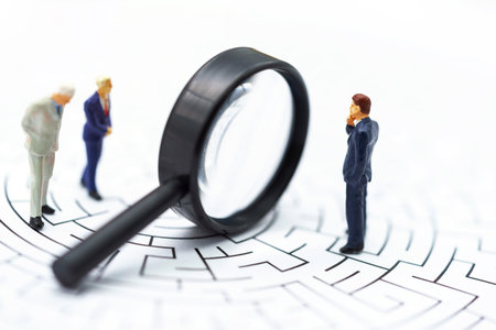 Miniature people: Businessman use magnifying glass to find the route on the maze. Concepts of finding a solution, problem solving and challenge.の写真素材