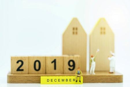 Miniature people: Businessman sitting on yellow block with house and number 2019.の写真素材