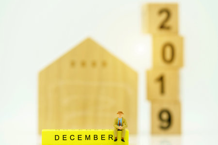 Miniature people: Businessman sitting on yellow block with house and number 2019.