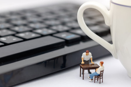 Miniature people sitting on table with keyboard and cup of coffee.
