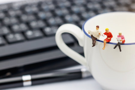 Miniature people sitting on cup of coffee with keyboard and pen.の写真素材