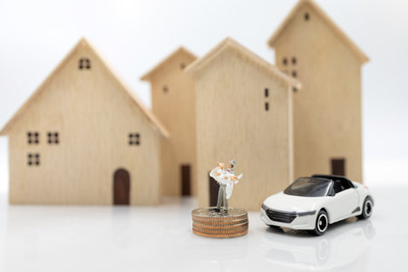 Miniature people: Couple in wedding dresses stand on coins stack with house and car. Family planning and housing concept.の写真素材