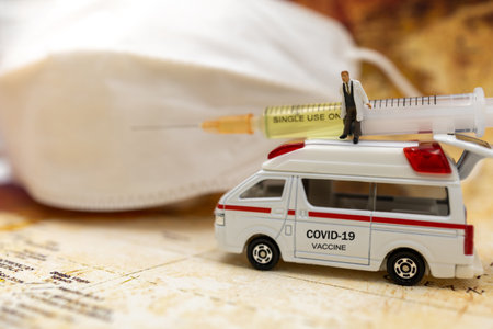 Miniature people stand on ambulance car with medical mask and Syringe of COVID-19 vaccine . Vaccine and Healthcare Medical concept.の写真素材