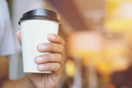 young man hand holding Paper cup of take away drinking coffee hot on cafe coffee shop.の写真素材