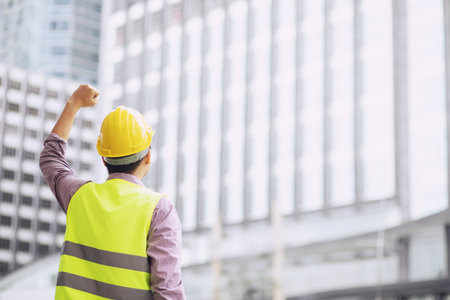 Close up backside view of engineering male construction worker stand holding safety white helmet for the safety of the work operation. outdoor of building background.の写真素材