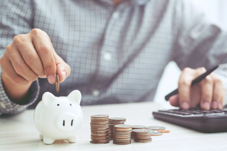 close up hand business man accounting with savings money coins stacked row with hand putting coins in jug glass. concept Write Finance accounting.の写真素材