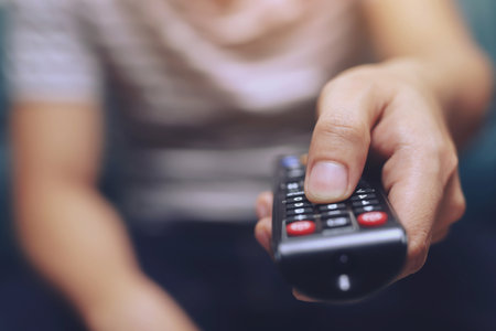 close up Television remote control in casual man hands pointing to tv set and turning it on or off. select channel watching tv on his sofa at home in the living room relax.の写真素材