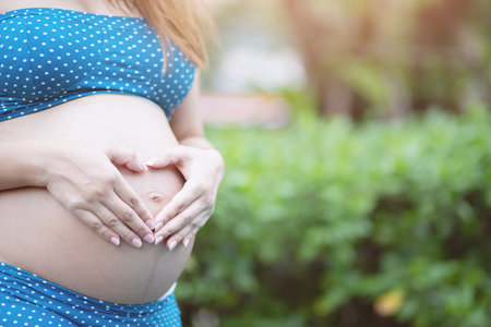 Pregnant woman in swimming suit underwear stand by the pool. use hand touch tummy belly with baby. Young woman expecting a baby Stand in the outdoors. Exercise to strengthen physical health Easy birthの写真素材