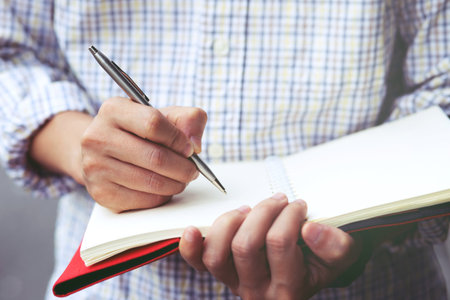 close up hand young man stand to using pen writing Record Lecture notepad into the book.の写真素材