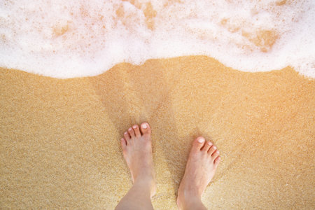 Closeup of a man's bare feet stand at wet on the beach , with a wave's edge foaming gently beneath them. Vacation on ocean beach, foot on sea sand. Leave empty copy space Enter the text above.の写真素材