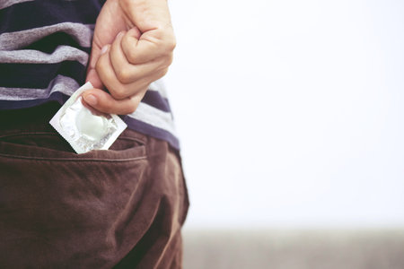 Young man jeans corduroy back side pocket to carry condoms taking in hand pick condom from jeans safe sex concept on the bed Prevent infection Contraceptive control the birth rate or safe prophylacticの写真素材