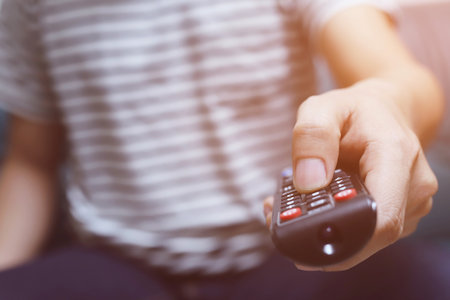 Close up young man using television remote control is sitting on a sofa. on or off tv.の写真素材