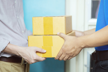 parcel delivery man of a package through a service. and close up hand customer accepting a delivery of boxes from delivery man postal send direct to home.の写真素材