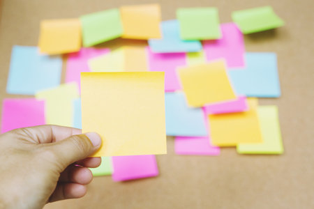 close up people holding paper post it in hand stick wall board. paper note colorful variety reminder sticky notes pin on cork bulletin board background. empty space for text.の写真素材