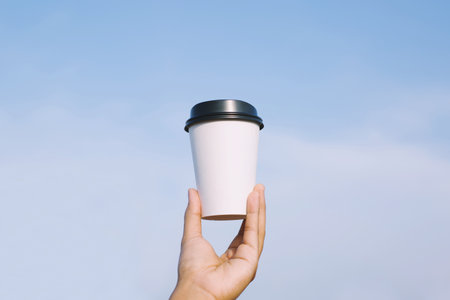 hand holding paper cup of take away drinking coffee on natural morning sunlight. space Place for your text or logo.の写真素材