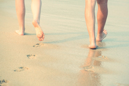 Closeup of a lady woman and man couple lover bare feet walking and footprint at wet on the beach romantic honeymoon. Vacation on ocean beach,foot on sea sand. Shadow from the sun hits the sand. travelの写真素材